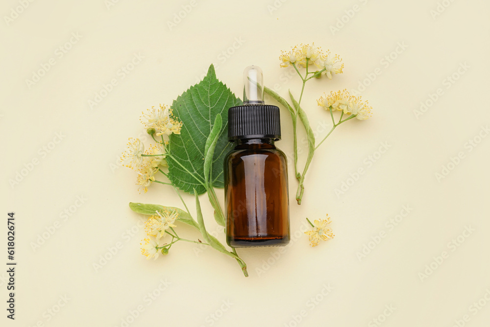 Bottle of essential oil and fresh linden flowers on color background