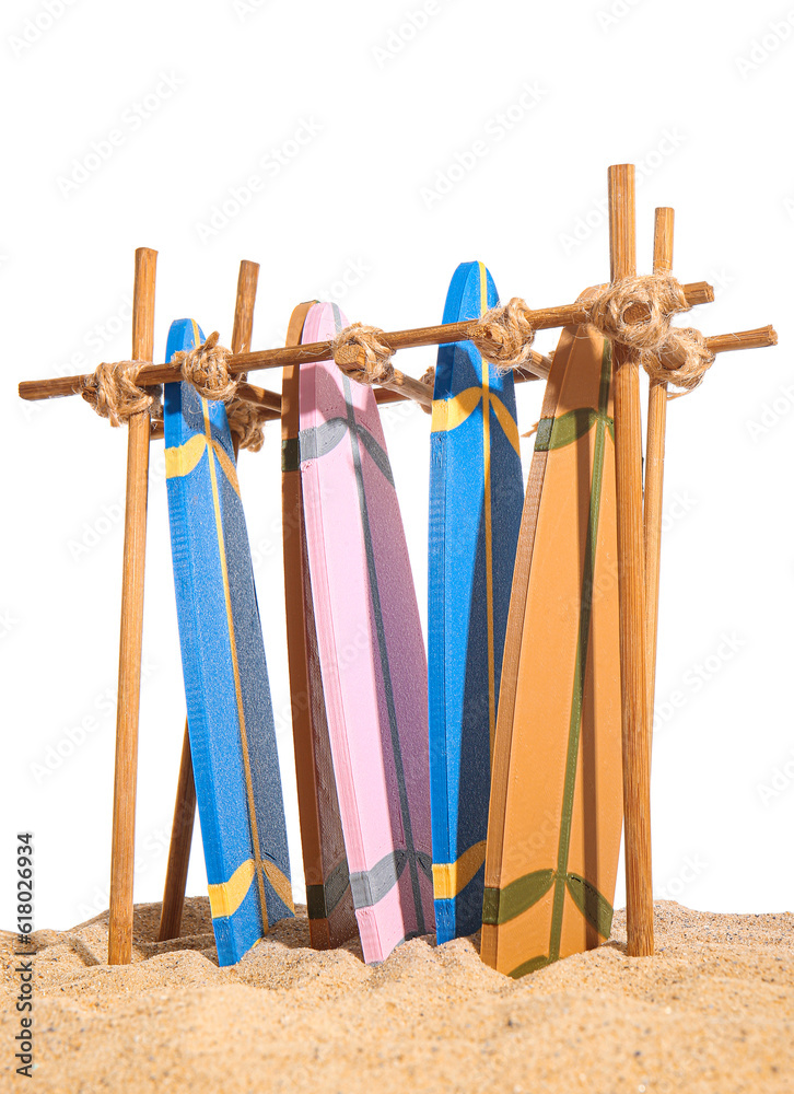 Stand with different mini surfboards on sand against white background