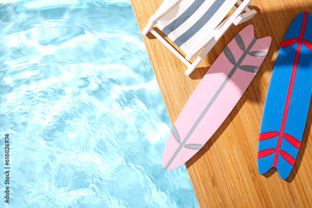 Creative composition with mini surfboards and deckchair on edge of swimming pool