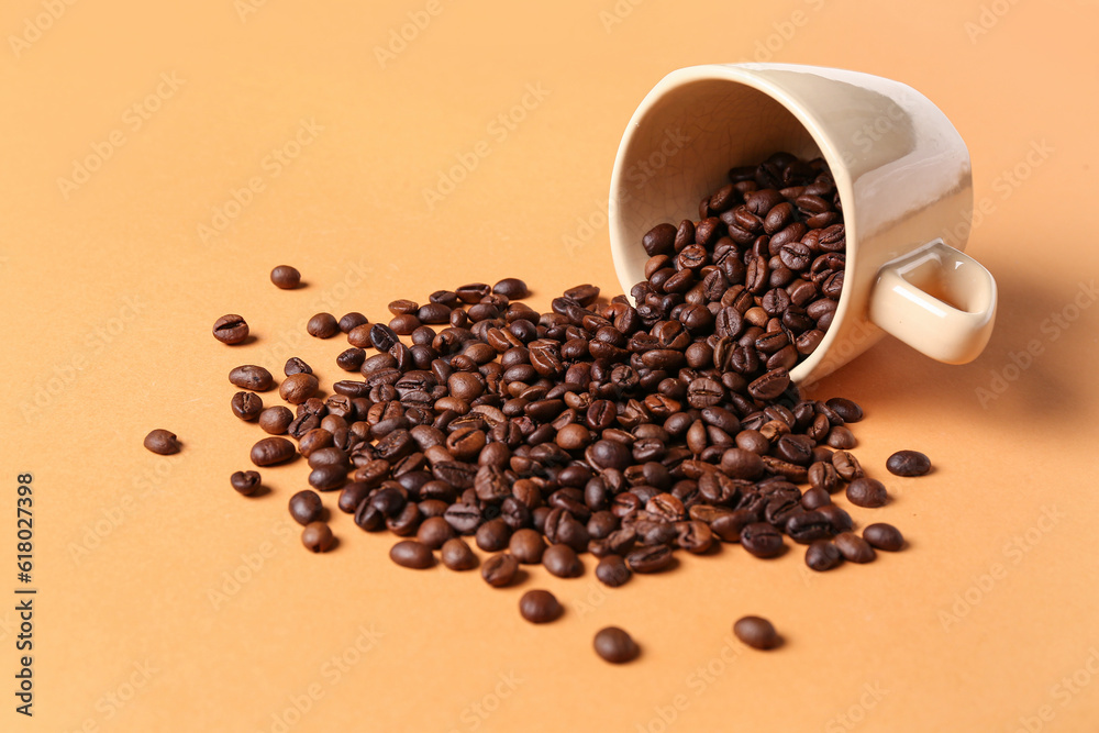 Overturned cup with coffee beans on orange background