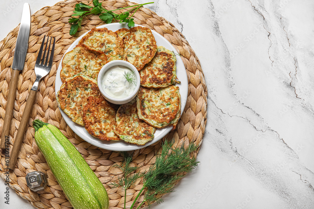 Plate of tasty zucchini fritters with sour cream on white marble background