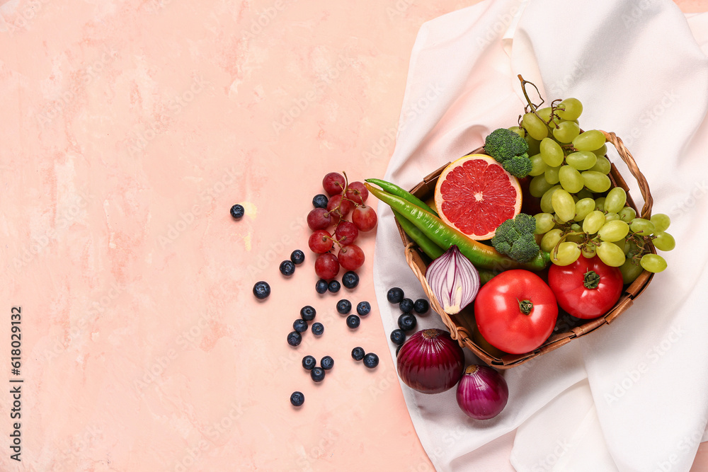 Wicker basket with different fresh fruits and vegetables on pink background