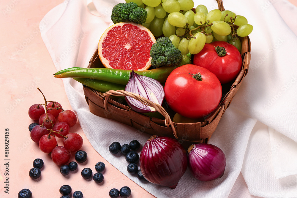 Wicker basket with different fresh fruits and vegetables on pink background