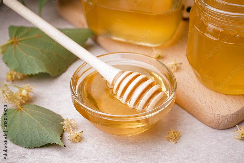 Glass bowl with linden honey and dipper on white background