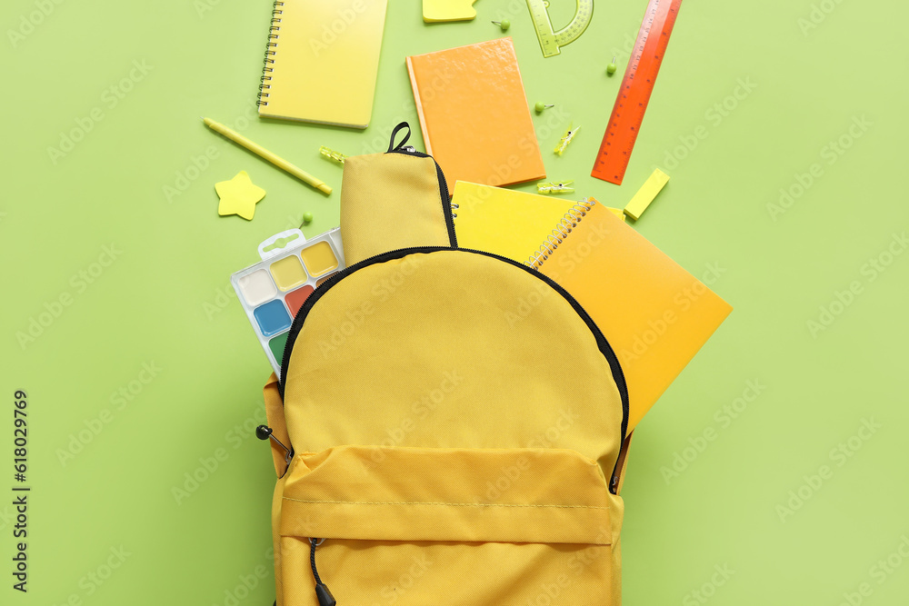 Yellow school backpack with notebooks, pencil case and watercolors on green background