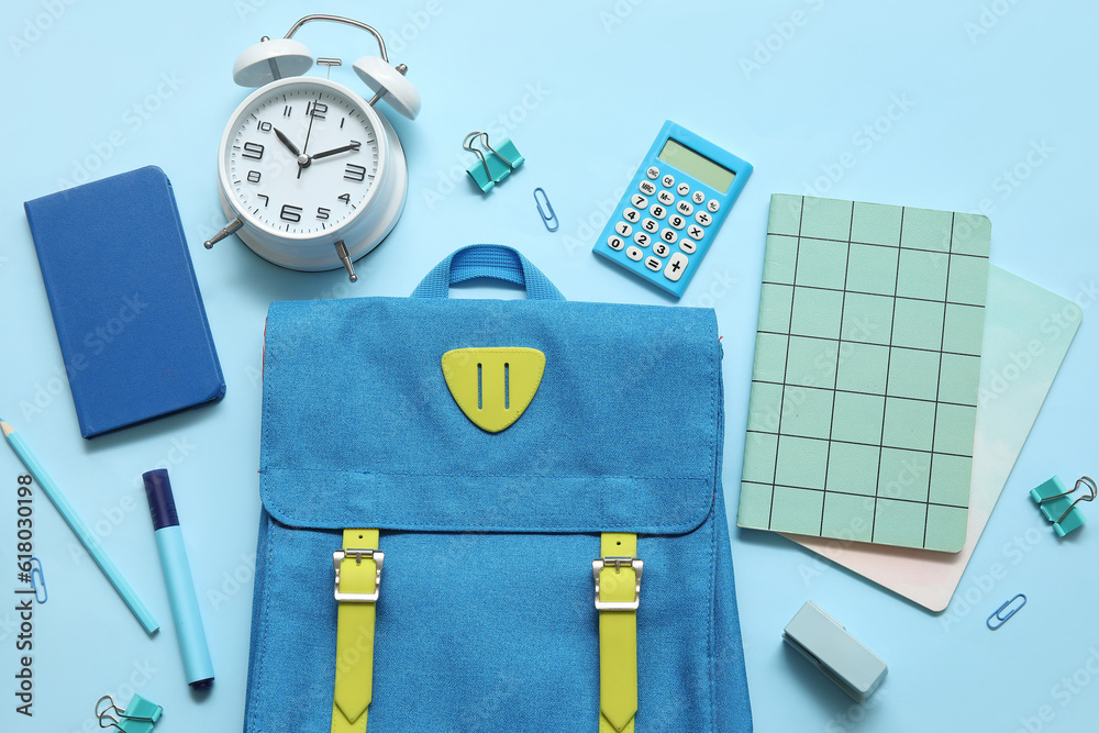 School backpack with notebooks, alarm clock and calculator on blue background