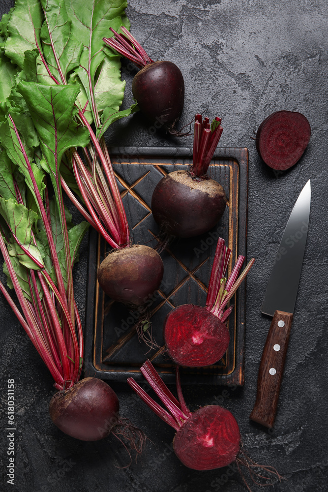 Wooden board of fresh beets with green leaves on black background