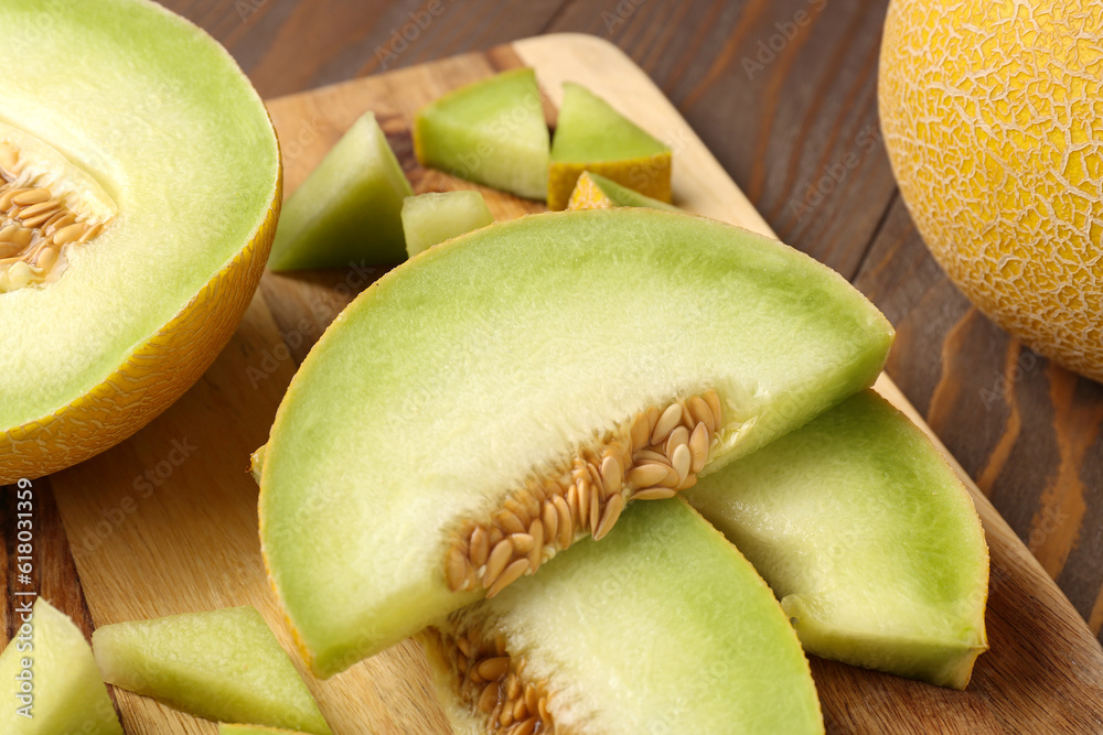 Board with pieces of sweet melon on wooden background, closeup