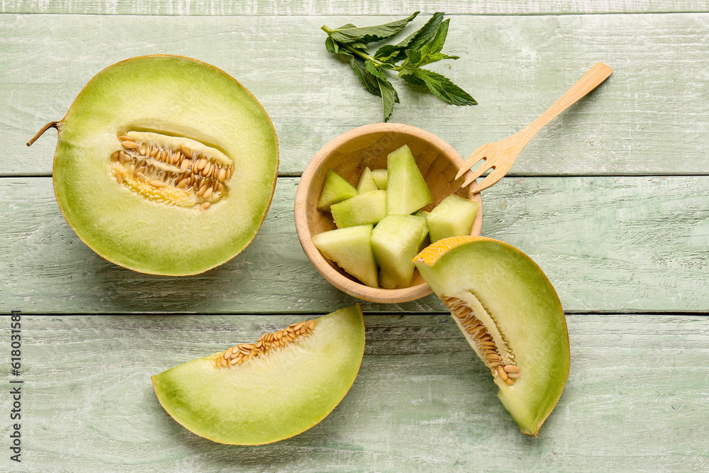 Half of sweet melon and bowl with pieces on green wooden background