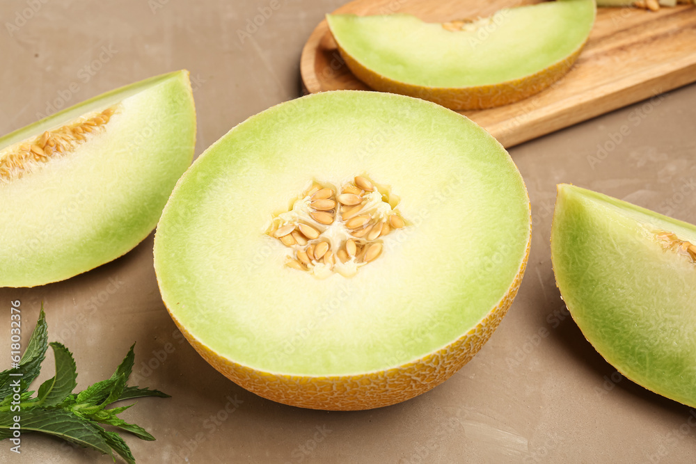 Half of sweet melon with pieces and mint on brown background