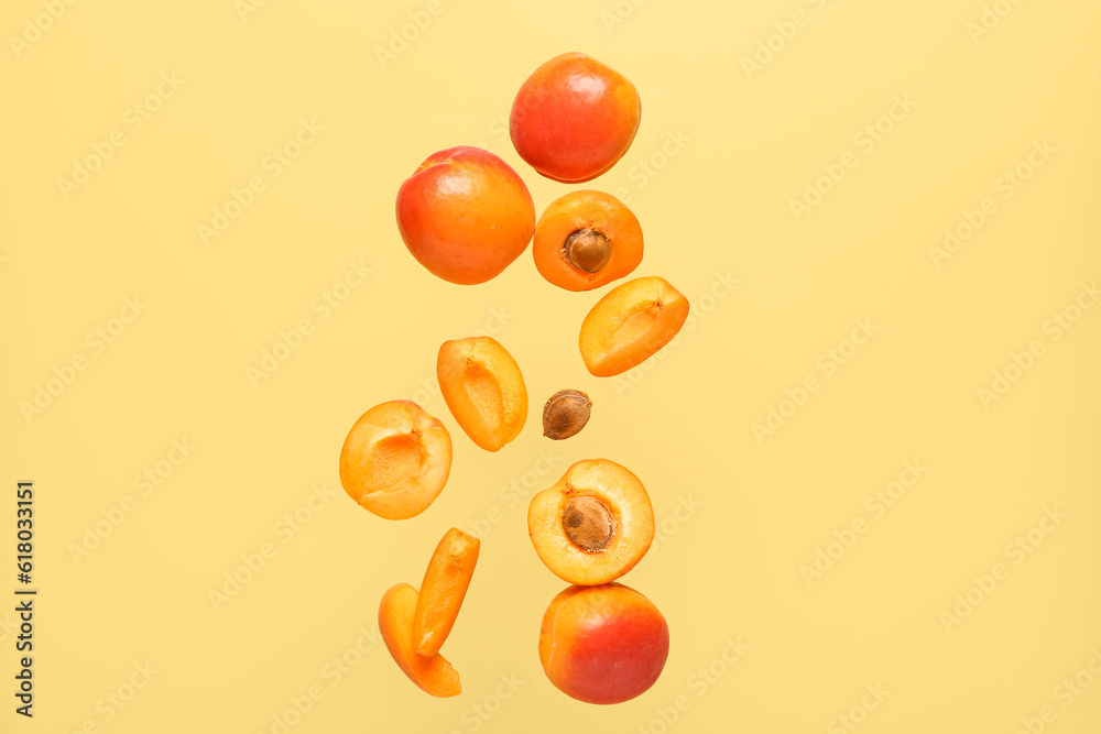 Flying fresh apricots with pieces on yellow background