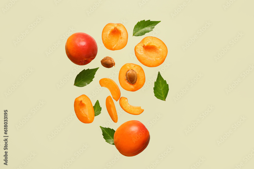 Flying fresh apricots with pieces and leaves on green background