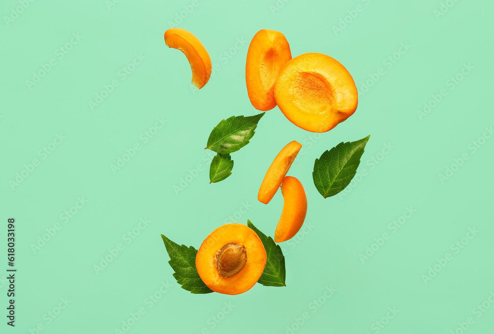 Flying halves of fresh apricot with pieces and leaves on turquoise background