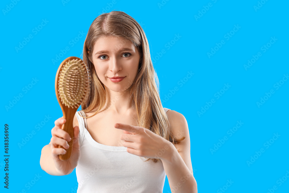 Young woman with hair loss problem pointing at brush on blue background