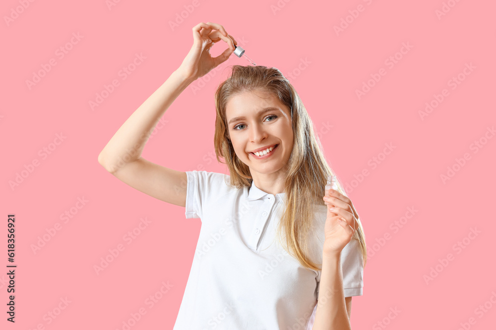 Young woman using serum for hair growth on pink background