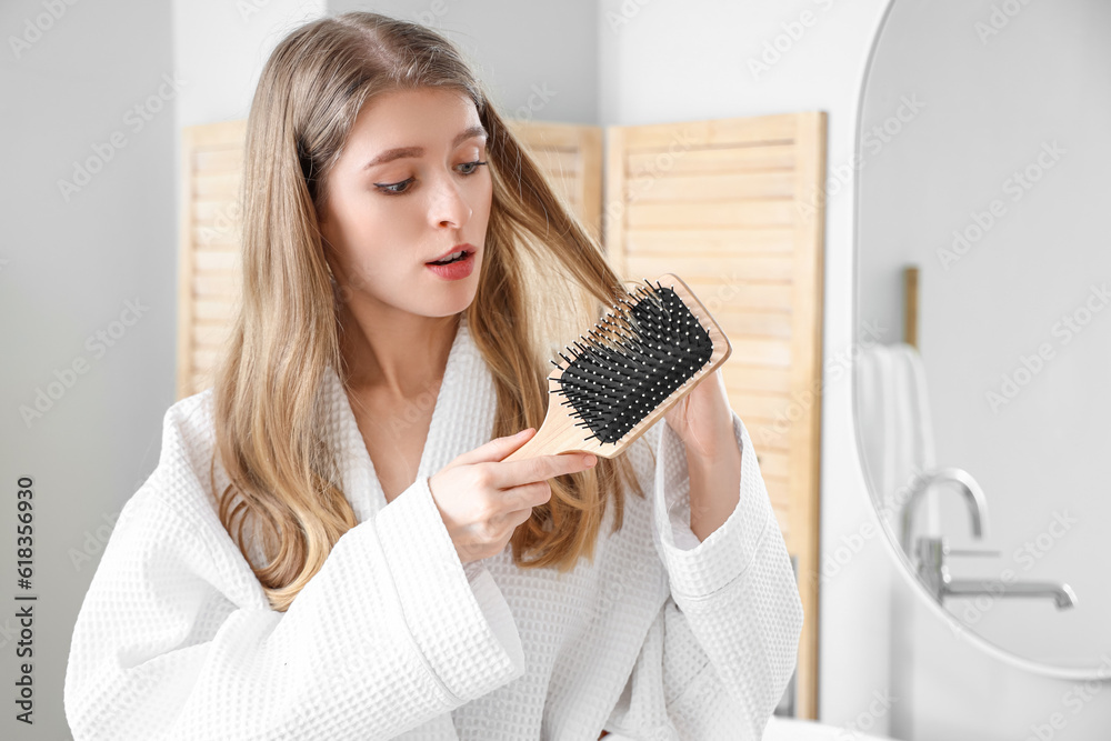 Young woman with hair loss problem brushing in bathroom