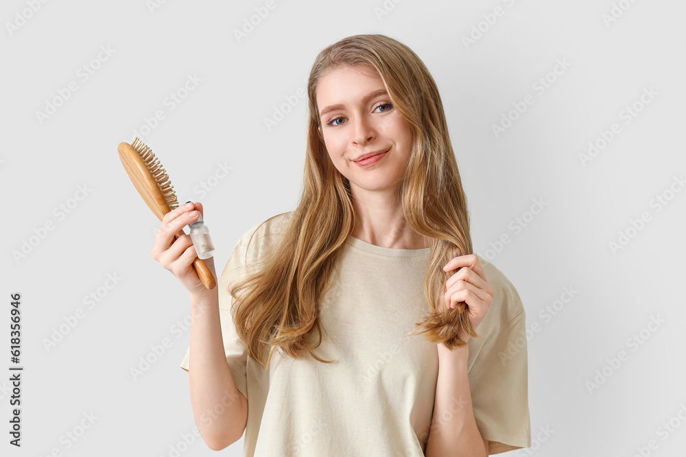 Young woman with serum for hair growth and brush on light background