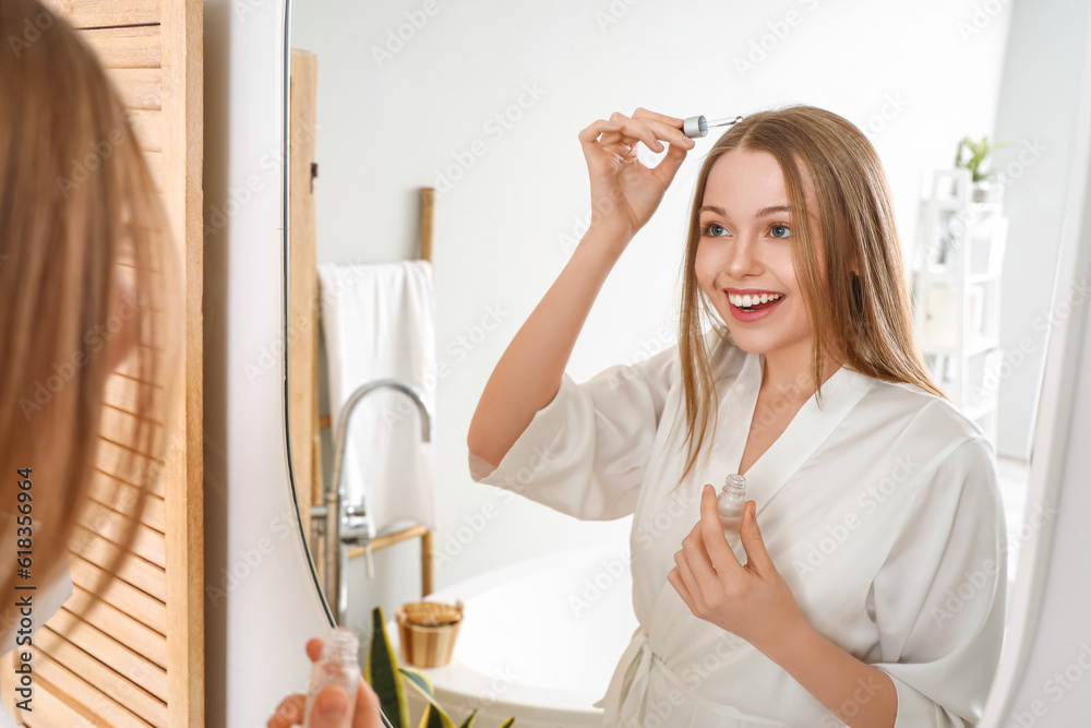 Young woman using serum for hair loss treatment at home