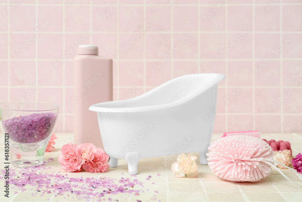 Composition with small bathtub, bath supplies and carnation flowers on color tile background