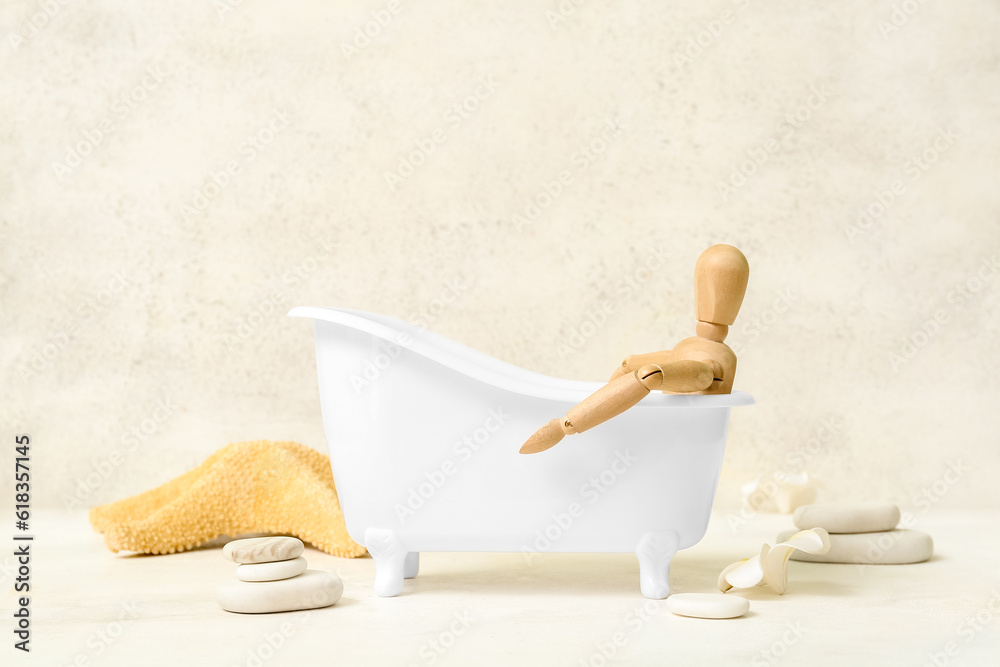 Small bathtub with wooden mannequin, spa stones and starfish on light background