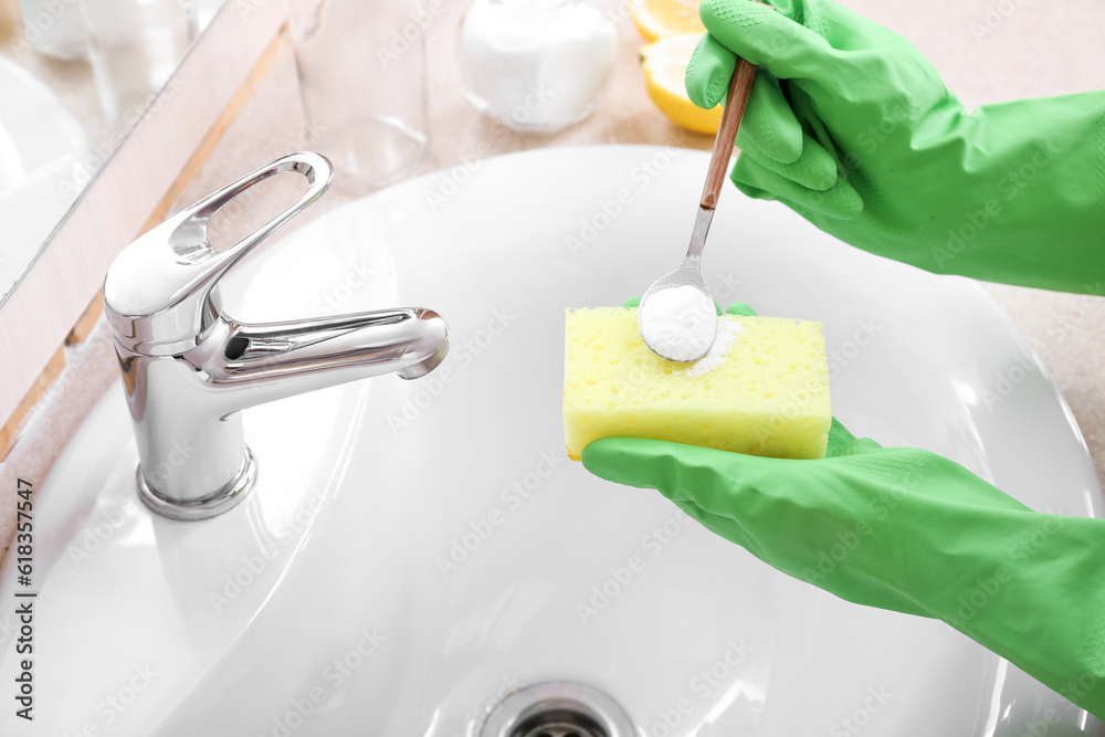 Woman in rubber gloves cleaning ceramic sink with sponge and baking soda, closeup