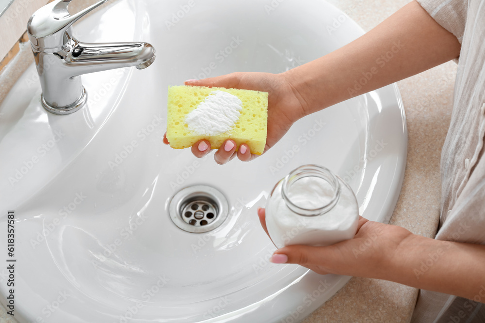 Woman cleaning sink with baking soda and sponge, closeup