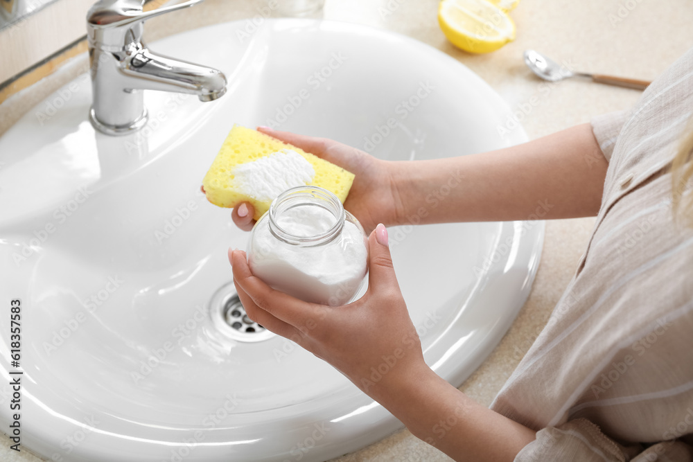 Woman cleaning sink with baking soda and sponge, closeup