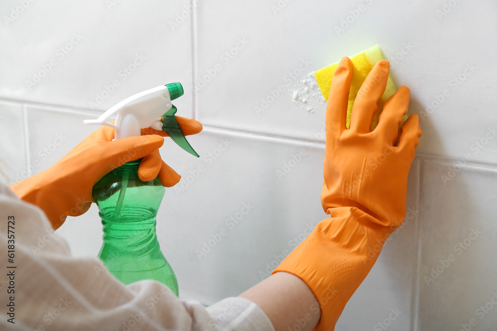 Woman in rubber gloves cleaning light tile with sponge, baking soda and sprayer, closeup