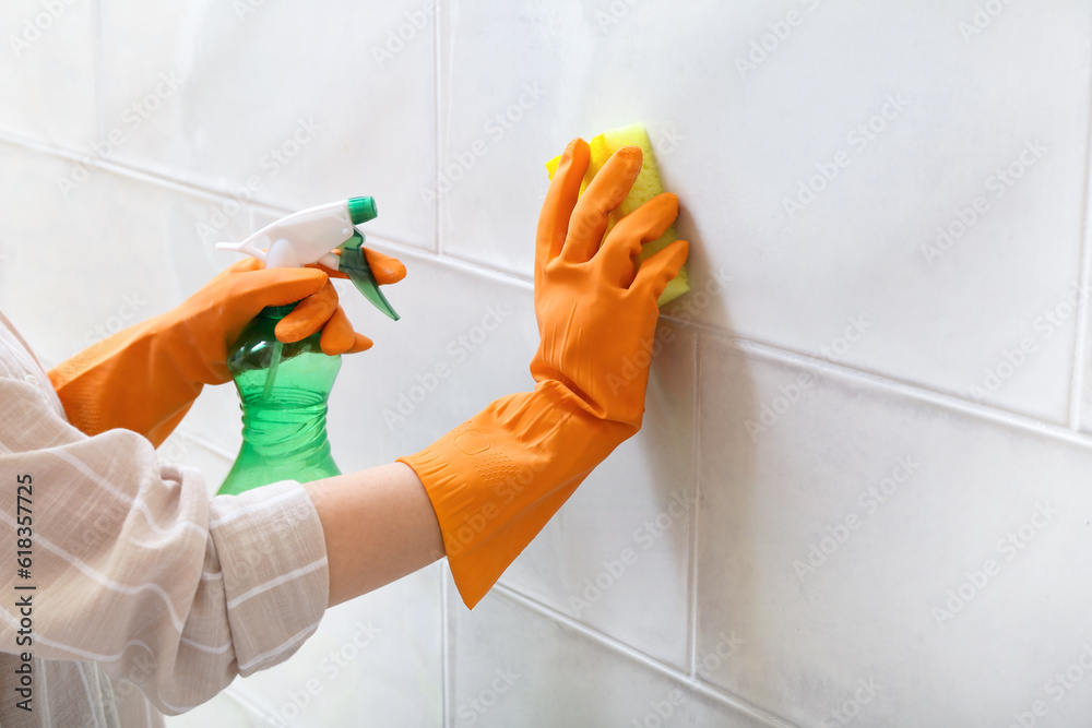 Woman in rubber gloves cleaning light tile with sponge, baking soda and sprayer