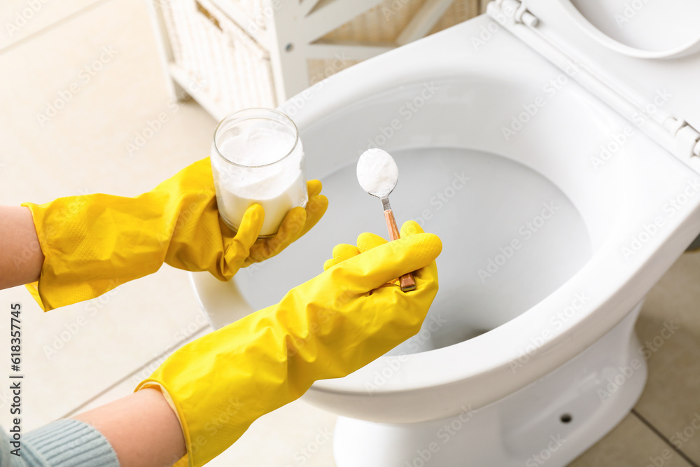 Woman in rubber gloves cleaning toilet bowl with baking soda