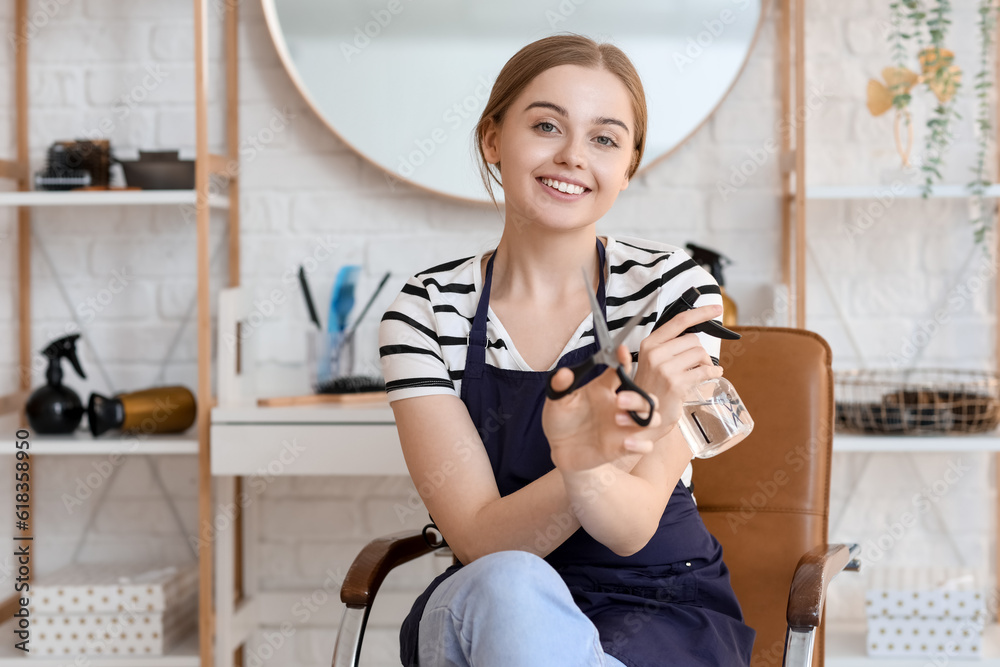 Female hairdresser with scissors and spray in beauty salon