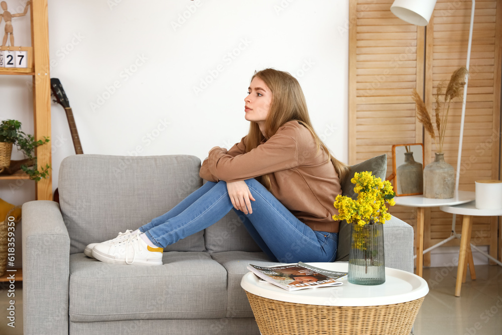 Thoughtful young woman sitting on sofa at home