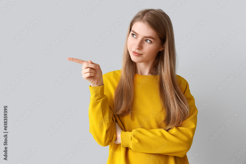 Thoughtful young woman pointing at something on light background