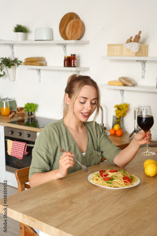 Young woman with glass of wine eating tasty pasta in kitchen