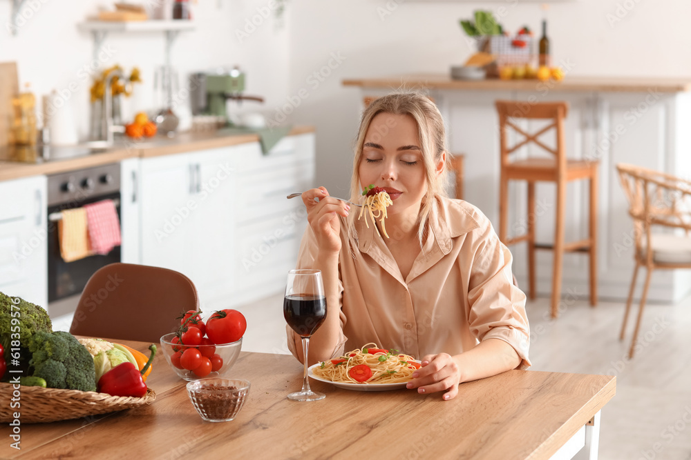 Young woman eating tasty pasta in kitchen