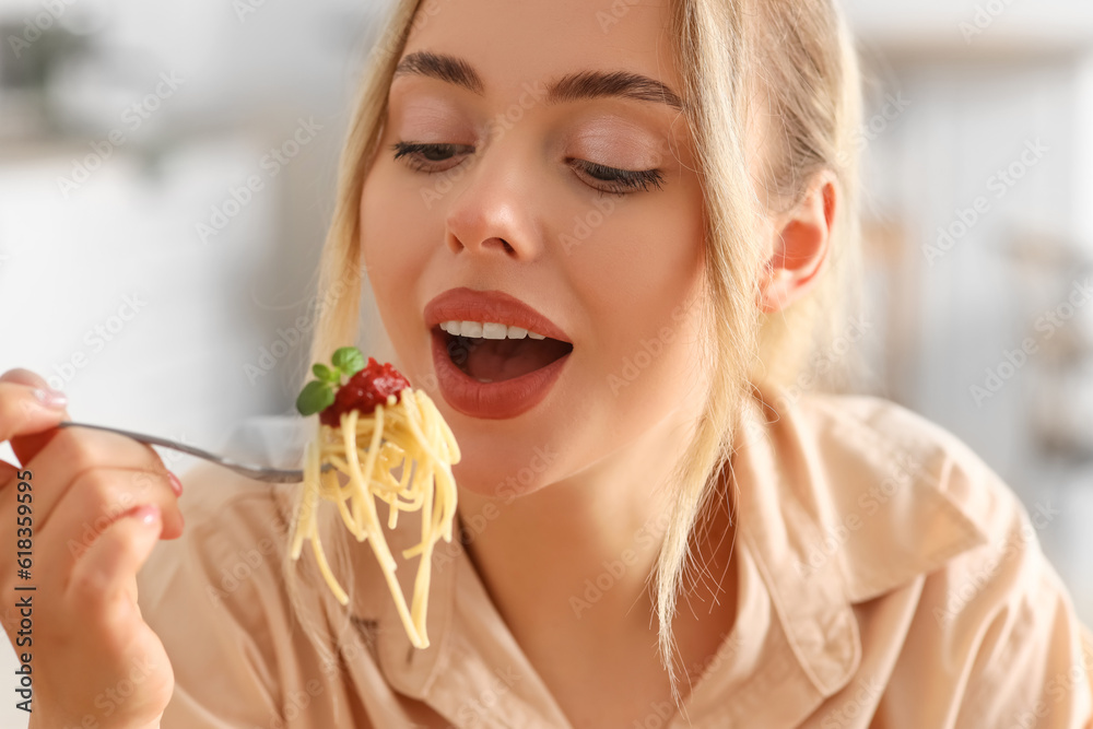 Young woman eating tasty pasta in kitchen, closeup