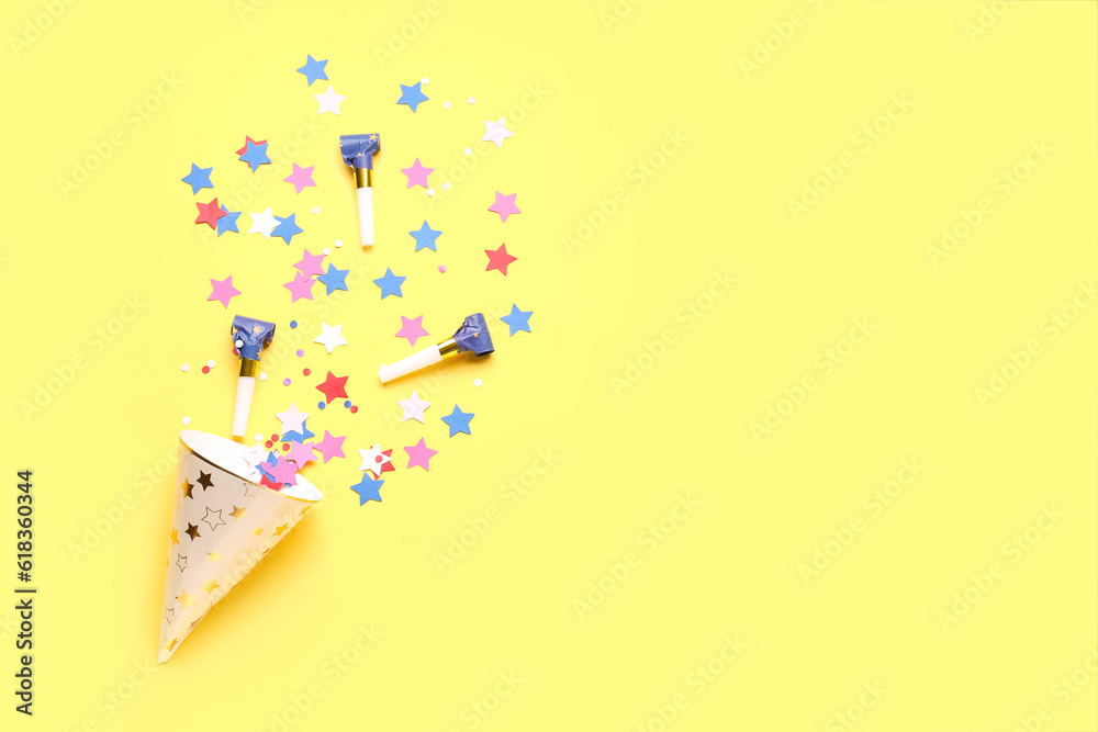 Composition with party hat and whistles on pale yellow background