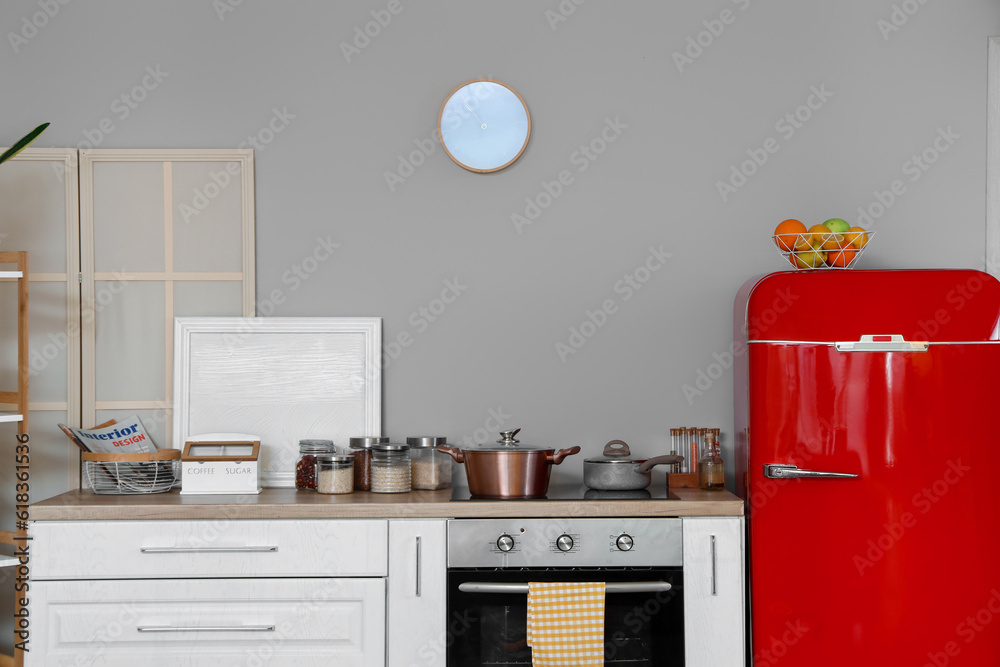 Interior of kitchen with red fridge, counters and clock hanging on light wall