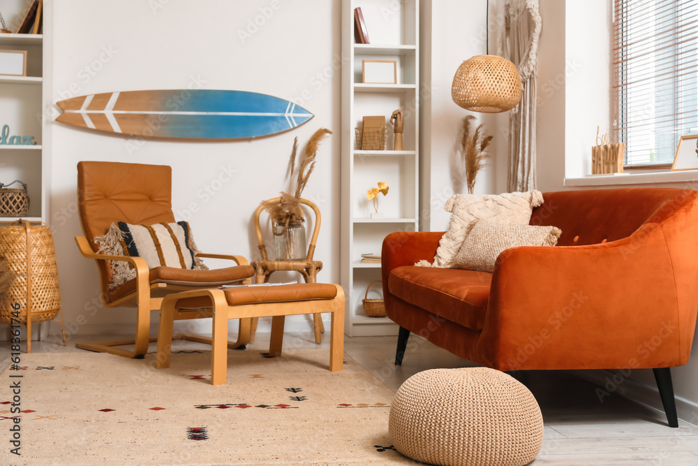 Interior of light living room with surfboard, brown sofa and armchair