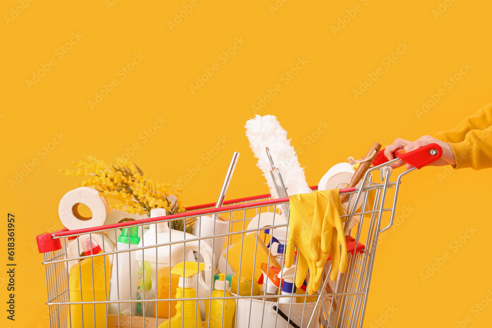 Woman with shopping cart full of cleaning supplies with flowers on yellow background