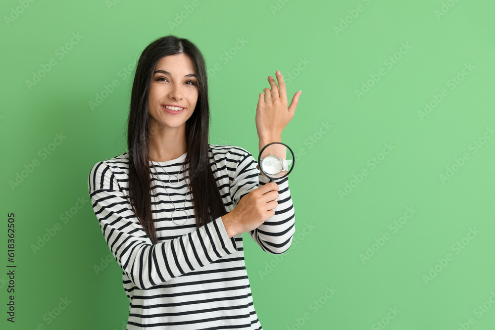 Beautiful happy young woman with magnifier and wristwatch on green background