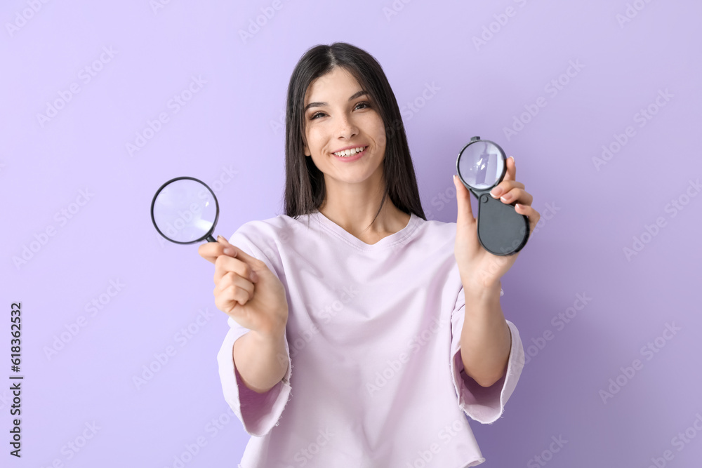 Beautiful happy young woman with magnifiers on lilac background