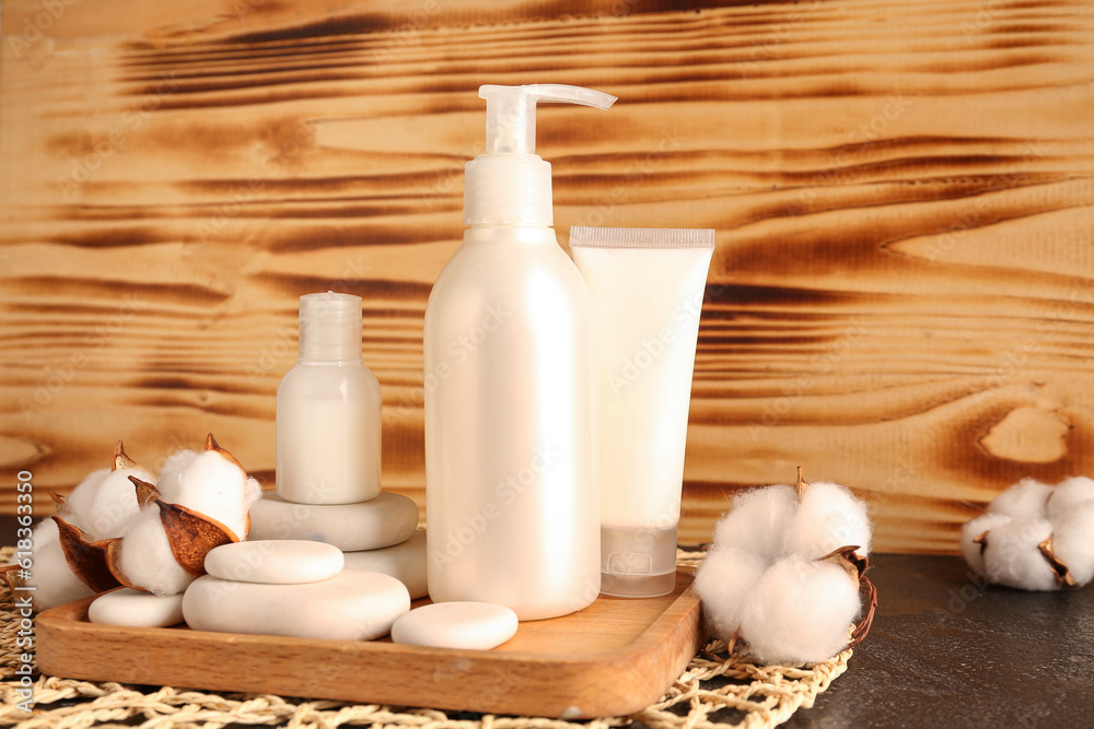 Bottles of cosmetic products, spa stones and cotton flowers on table against wooden background