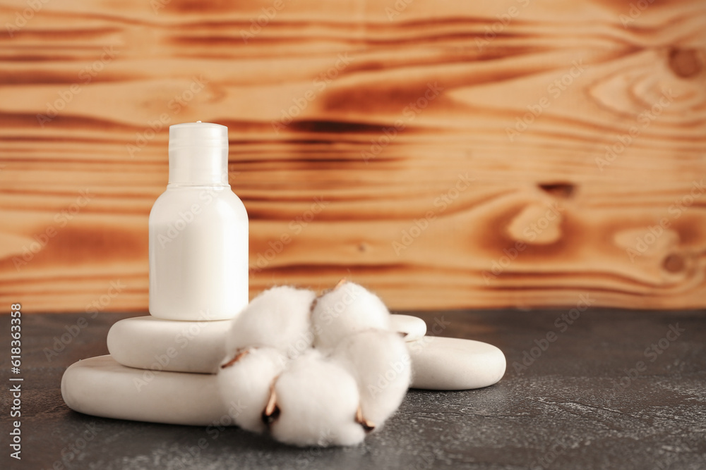 Bottle of cosmetic product and cotton flower on dark table against wooden background