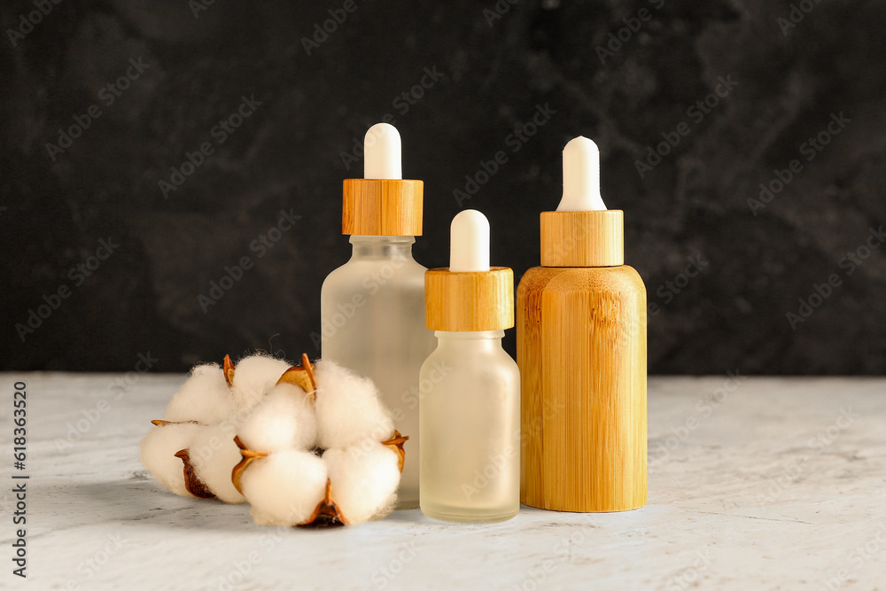 Bottles of essential oil and cotton flowers on light table