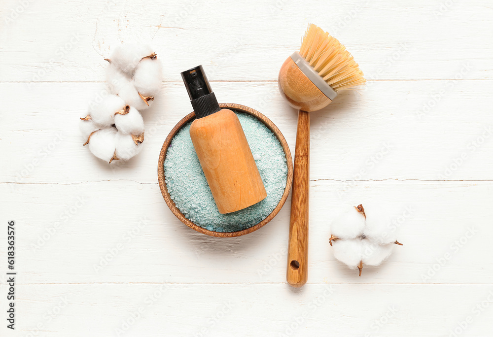 Bottle of cosmetic product, sea salt, massage brush and cotton flowers on light wooden background