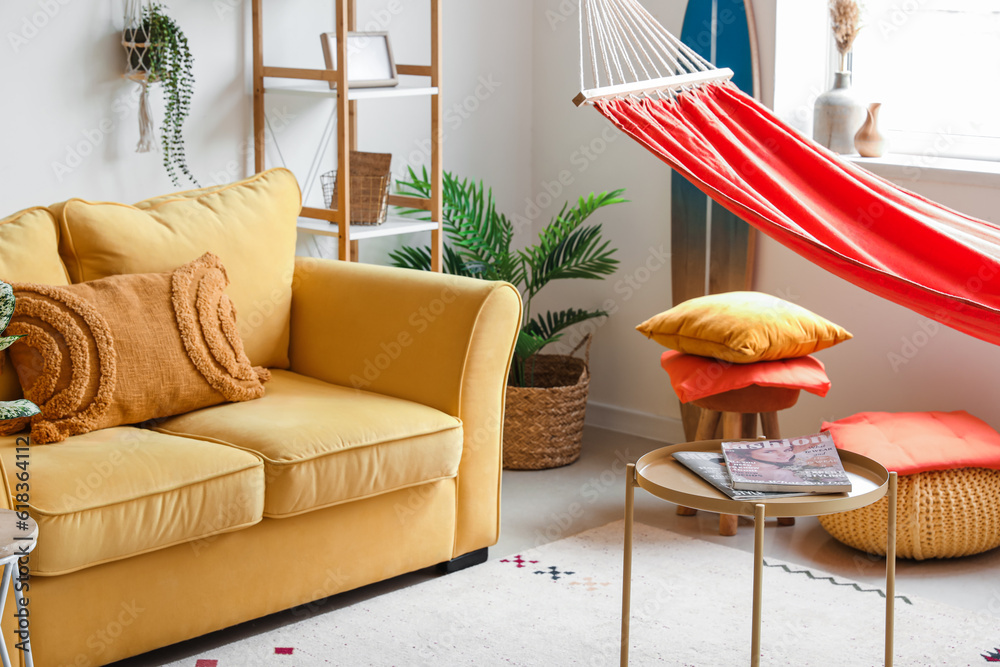 Interior of stylish living room with red hammock, yellow sofa and coffee table