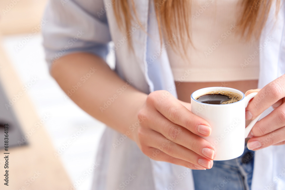 Woman holding cup of delicious coffee in kitchen