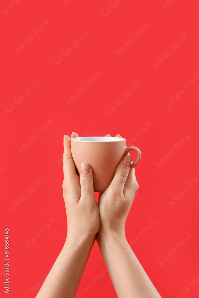 Female hands holding cup of red background