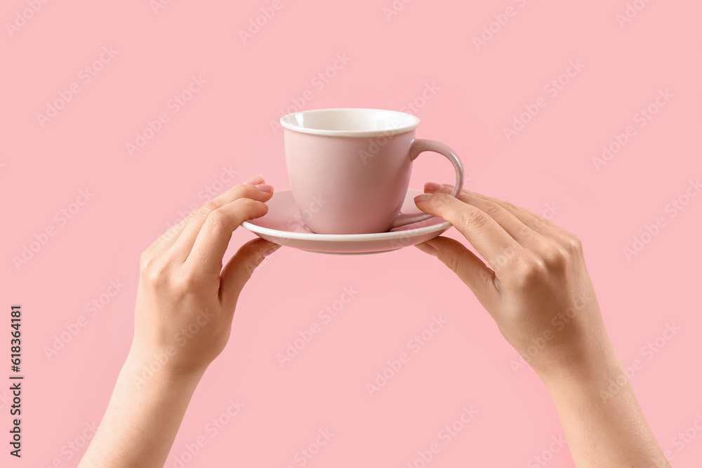 Female hands holding cup and saucer on pink background